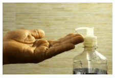 Photographie de deux mains ouvertes recevant du gel hydroalcoolique versé depuis un flacon pompe posé à droite.
