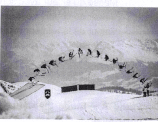 Photographie en noir et blanc d'un saut de ski freestyle : les positions successives du skieur, superposées sur une même image, décrivent une trajectoire en cloche au-dessus d'un tremplin, sur fond de montagne enneigée.