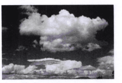 Photographie en noir et blanc d'un ciel nuageux : de gros cumulus aux contours découpés se détachent au-dessus d'une bande de nuages plus bas.